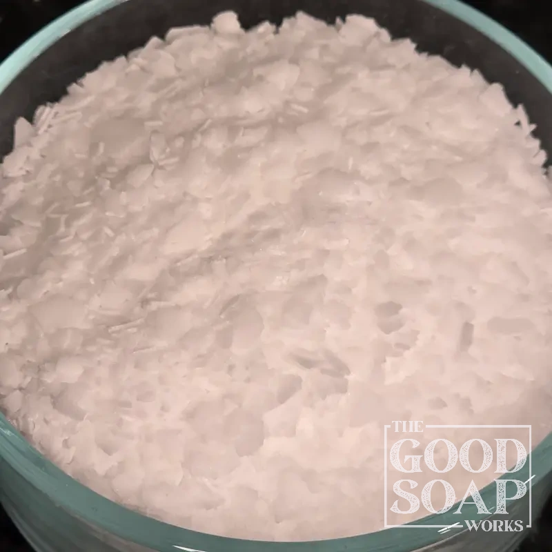 Stearic acid flakes on a spoon — a plant-derived fatty acid used as a hardener in natural soap making
