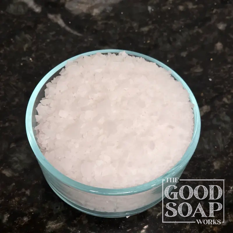 Close-up of Magnesium Chloride flakes on a spoon, an ingredient used in soap and skincare by The Good Soap Works Co.