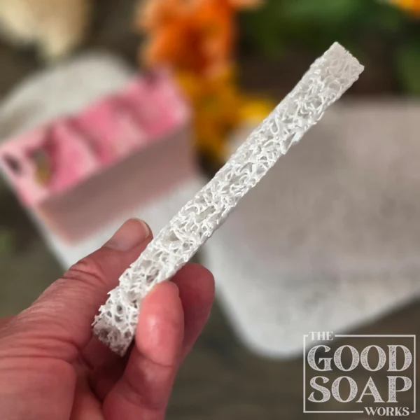 Light grey plastic soap saver pad with a handmade bar of soap resting on its textured open surface and a closeup view of the thickness of the pad