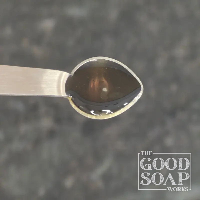 Tamanu oil on a wooden spoon — a rich, dark botanical oil used in natural skincare and soap making